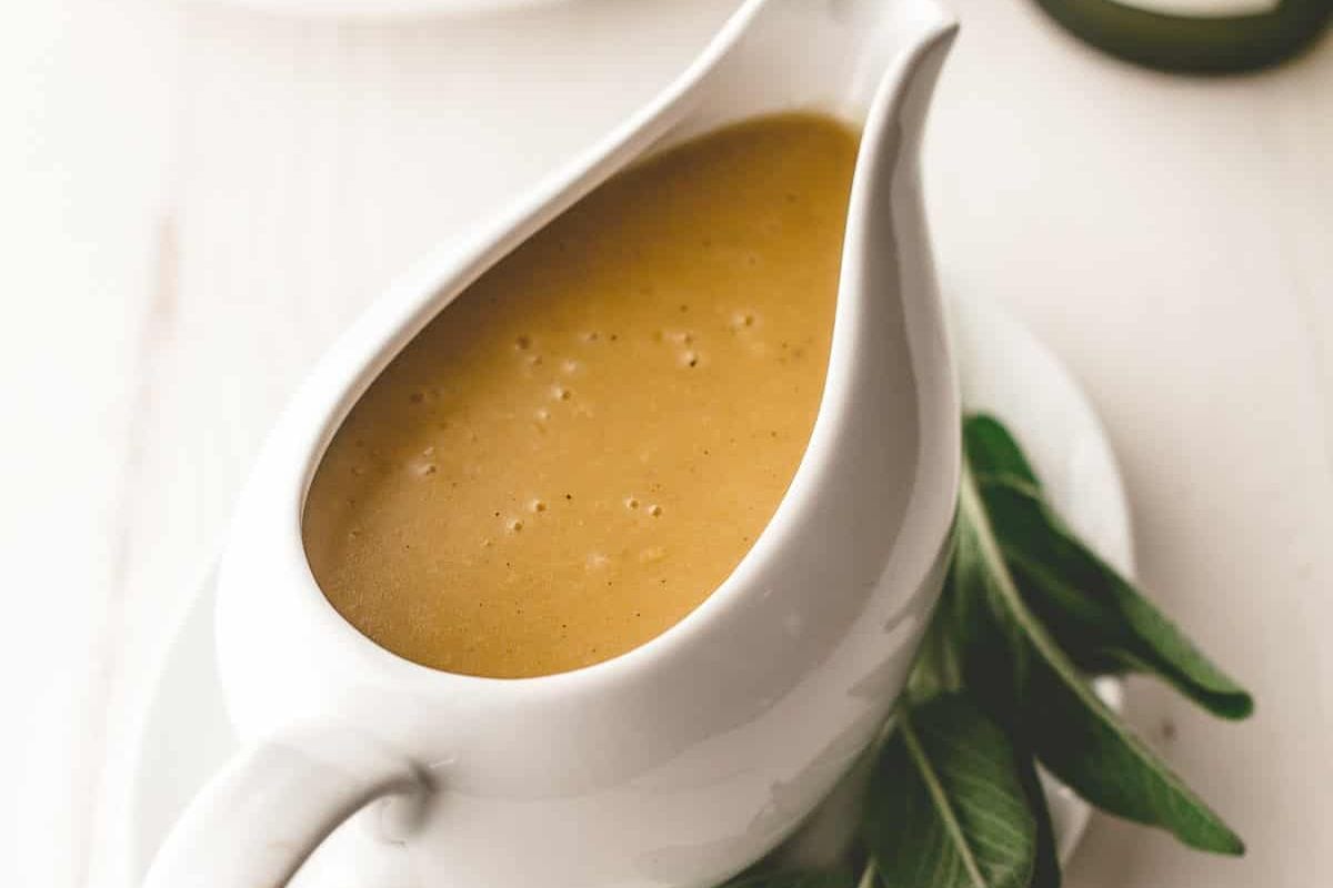 Close-up view of a creamy turkey gravy served in an elegant white sauce boat with fresh herbs on the side