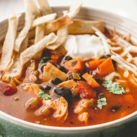 A bowl of chicken tortilla soup garnished with tortilla strips, sour cream, and fresh cilantro, served on a wooden table.