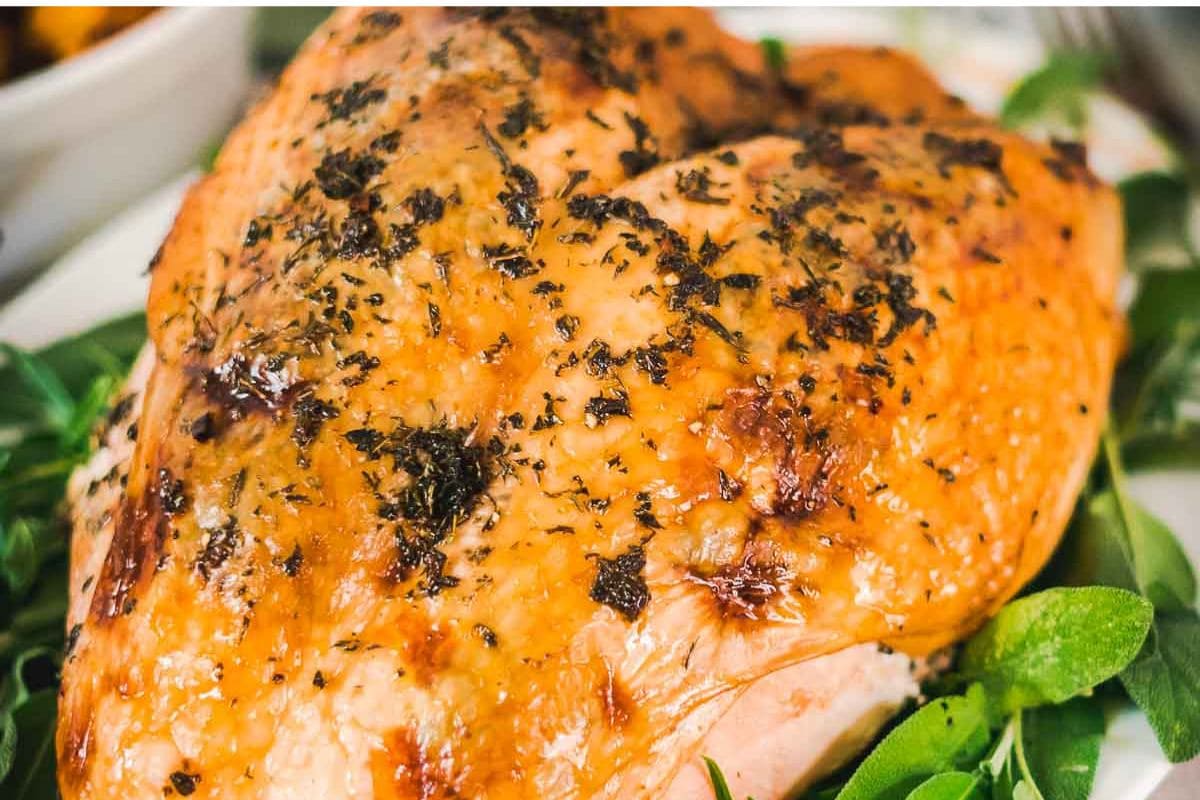 Close-up of a seasoned roasted turkey breast with herbs on a bed of greens.