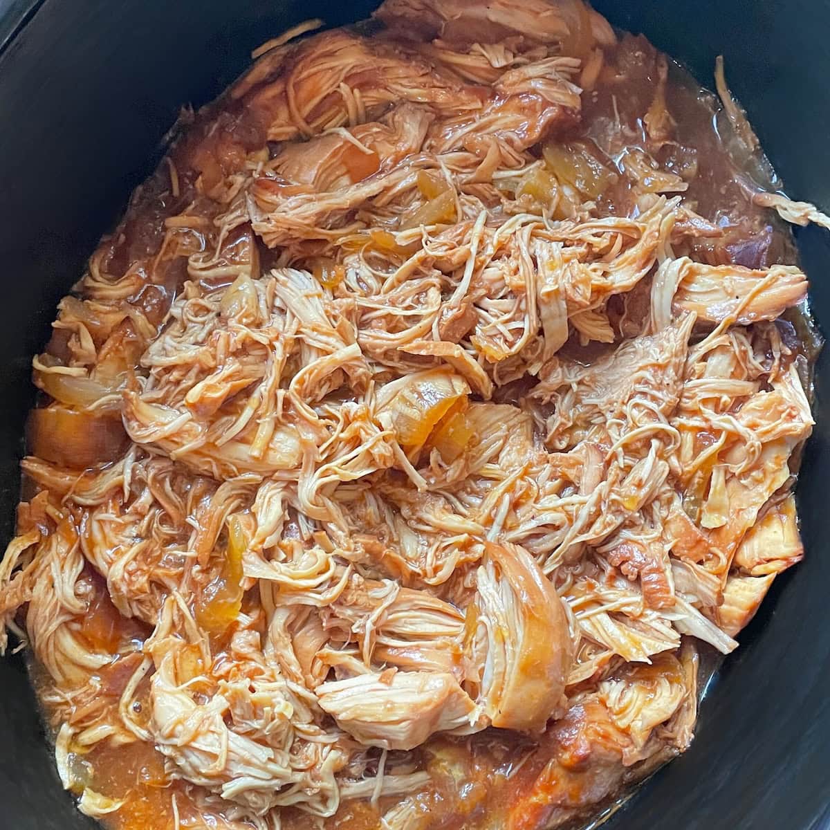 A close-up view of shredded chicken with sauce in a crockpot.