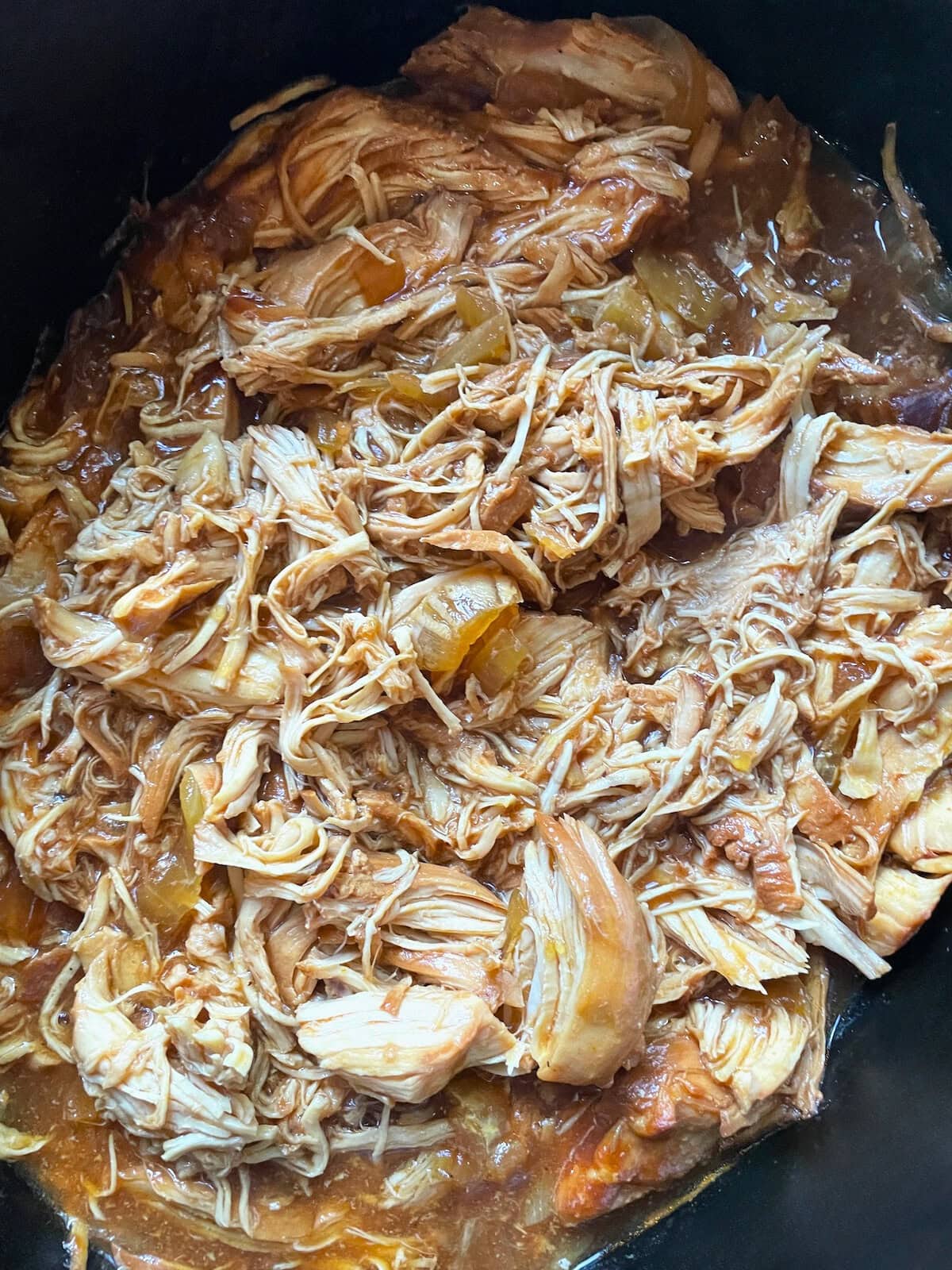 A close-up view of shredded chicken with barbecue sauce in a crockpot.