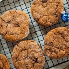 Aerial view of homemade ginger cookies with cracked tops cooling on a wire rack, with a decorative blue Christmas ornament on the side.