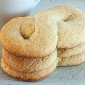 A stack of homemade sugar cookies sprinkled with sugar close to a white mug on a wooden surface.