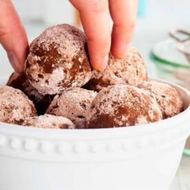 A hand picking a rum ball from a white bowl filled with rum balls.