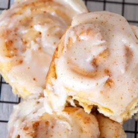 Close-up of cinnamon rolls with white icing, sitting on a wire cooling rack.