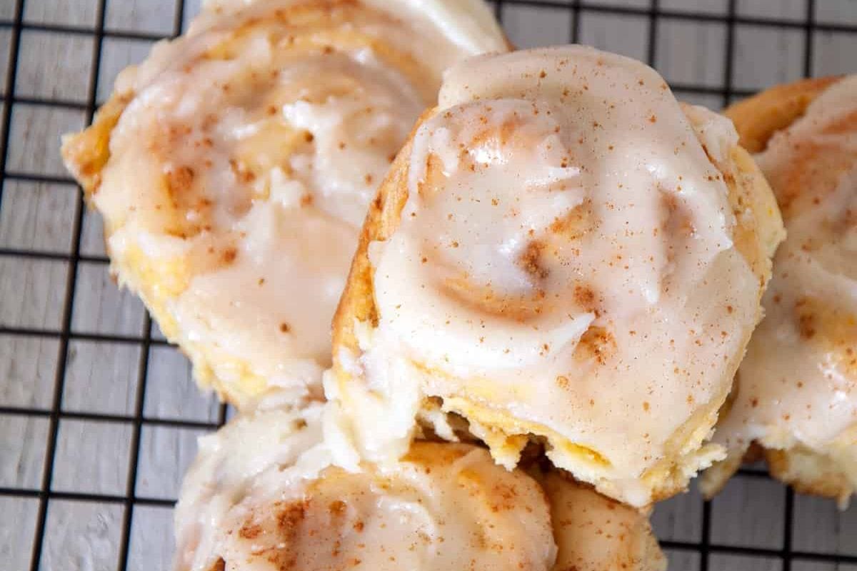 Close-up of cinnamon rolls with white icing, sitting on a wire cooling rack.