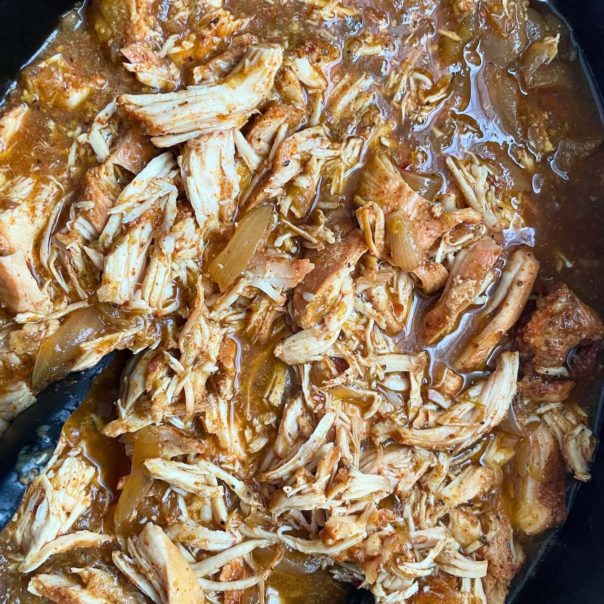 A close-up view of chicken and onions cooked in salsa verde with taco seasoning in a slow cooker.