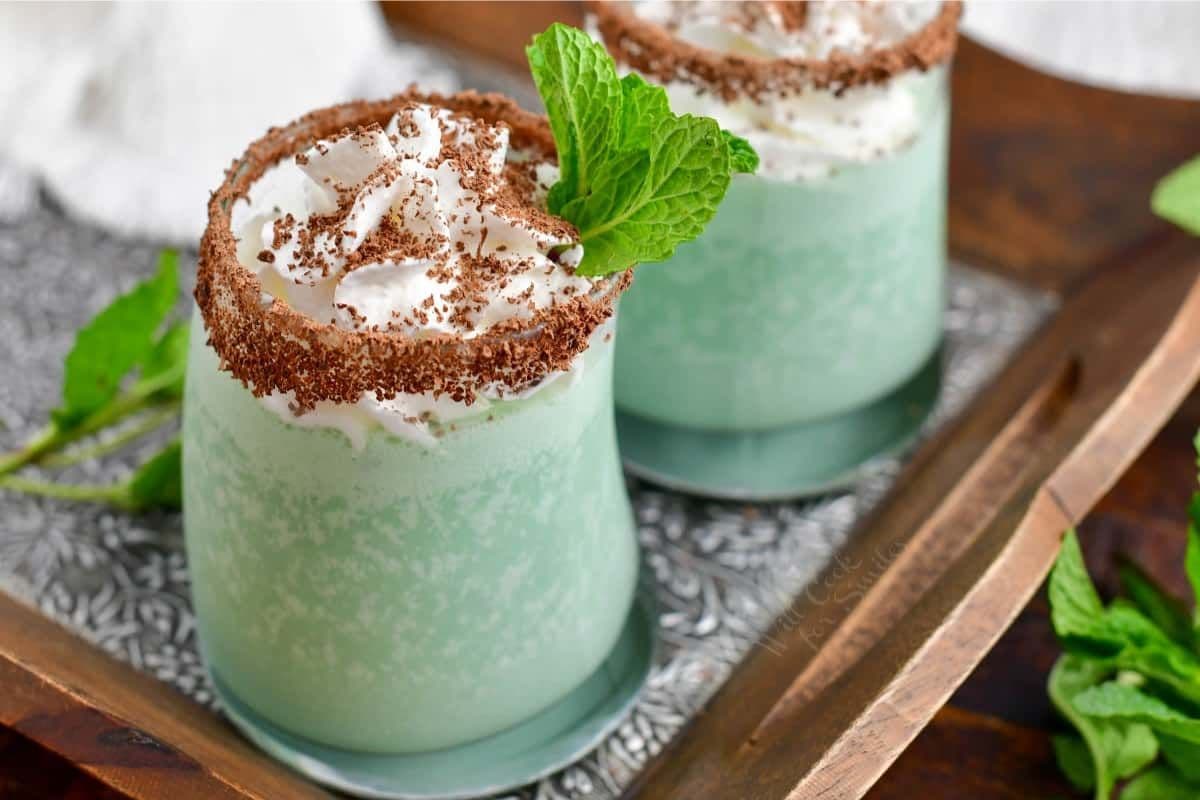 A refreshing mint green beverage topped with whipped cream, chocolate shavings, and a mint leaf, served in a decorative glass.