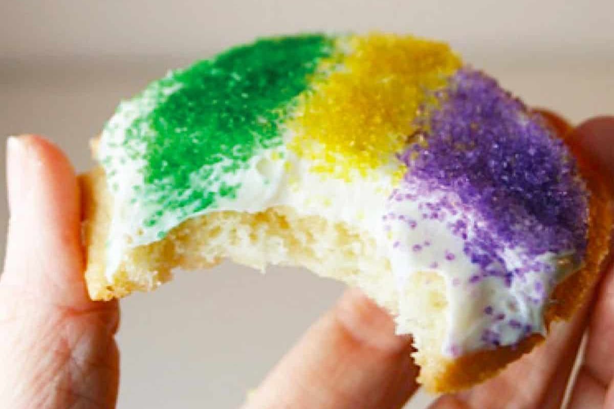 A hand holding a festive cookie topped with vibrant green, yellow, and purple sprinkles, showcasing a bite taken out.