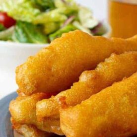 A close-up of golden battered fish sticks served with a side of fresh salad and a small bowl of tartar sauce.