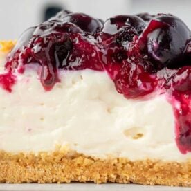 A close-up view of a slice of creamy cheesecake topped with a rich berry compote, showcasing a golden graham cracker crust.