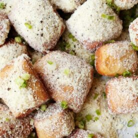 A close-up of golden-brown, crispy cheese-stuffed bites coated in a sprinkle of seasoning and green onions.