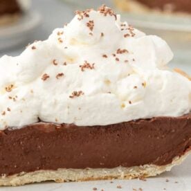 A decadent slice of chocolate cream pie topped with fluffy whipped cream and chocolate shavings, set on a light plate.