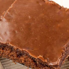 Close-up of a rich chocolate frosted brownie slice on a spatula, showcasing its fudgy texture and glossy icing.