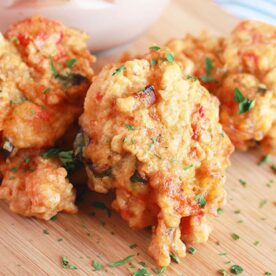 Close-up of crispy fritters garnished with parsley, served on a wooden platter with a side of dipping sauce.