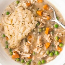 A bowl of creamy chicken and dumplings featuring tender chicken, carrots, peas, and fluffy dumplings in a savory broth.
