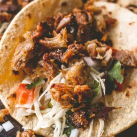 Close-up of tacos filled with seasoned meat, fresh vegetables, and herbs, served on soft tortillas.