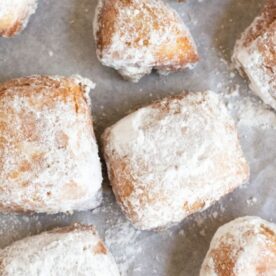 Freshly made beignets coated in powdered sugar, arranged beautifully on parchment paper.