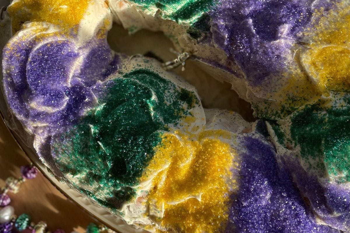 Close-up of a colorful Mardi Gras king cake topped with green, yellow, and purple sugar sprinkles.