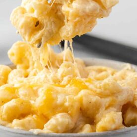 A close-up of creamy macaroni and cheese with melted cheese stretching as it is lifted from a bowl.