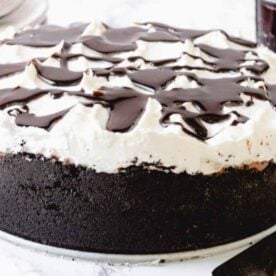A luscious chocolate cream cake topped with whipped cream and drizzled with chocolate syrup, set against a marble background.