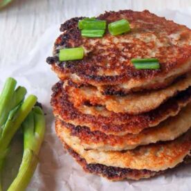 A stack of golden-brown potato pancakes garnished with green onions, alongside fresh green onions.