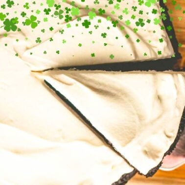 A close-up of a sliced chocolate cream pie topped with a smooth layer of cream, decorated with scattered green shamrock icons for a festive touch.