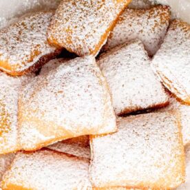 A tempting pile of freshly made beignets sprinkled with powdered sugar, resting on parchment paper.