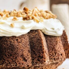 A close-up view of a chocolate cake topped with cream cheese frosting and sprinkled with chopped walnuts.
