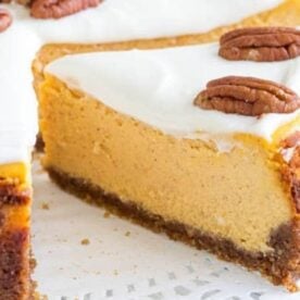 A slice of pumpkin cheesecake topped with cream cheese frosting and pecans, showcasing a smooth orange filling and a golden crust.