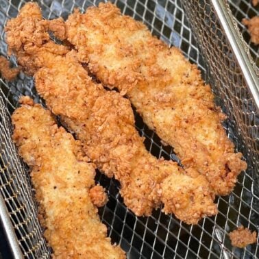 Golden-brown fried chicken tenders resting in a wire basket, showcasing their crunchy coating.