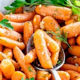 A close-up view of flavorful roasted baby carrots garnished with herbs and a spoon for serving.