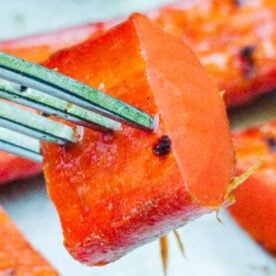 A close-up of a fork holding a vibrant piece of grilled sweet potato with several more pieces in the background.