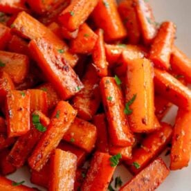 A plate of roasted glazed carrots garnished with fresh parsley, showcasing their vibrant orange color and caramelized edges.