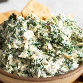 A close-up view of creamy spinach dip served in a bowl, accompanied by crunchy crackers for dipping.