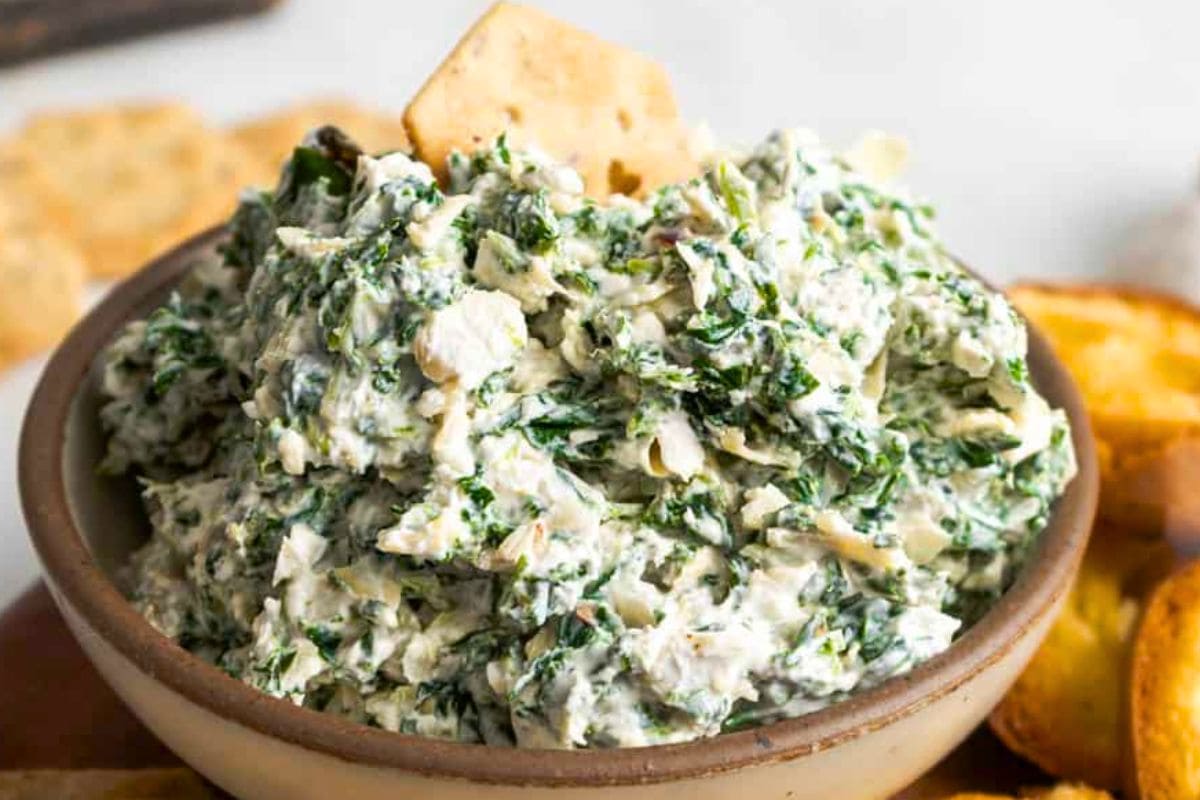 A close-up view of creamy spinach dip served in a bowl, accompanied by crunchy crackers for dipping.