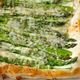 A golden puff pastry topped with fresh asparagus and melted cheese, garnished with herbs and pepper.