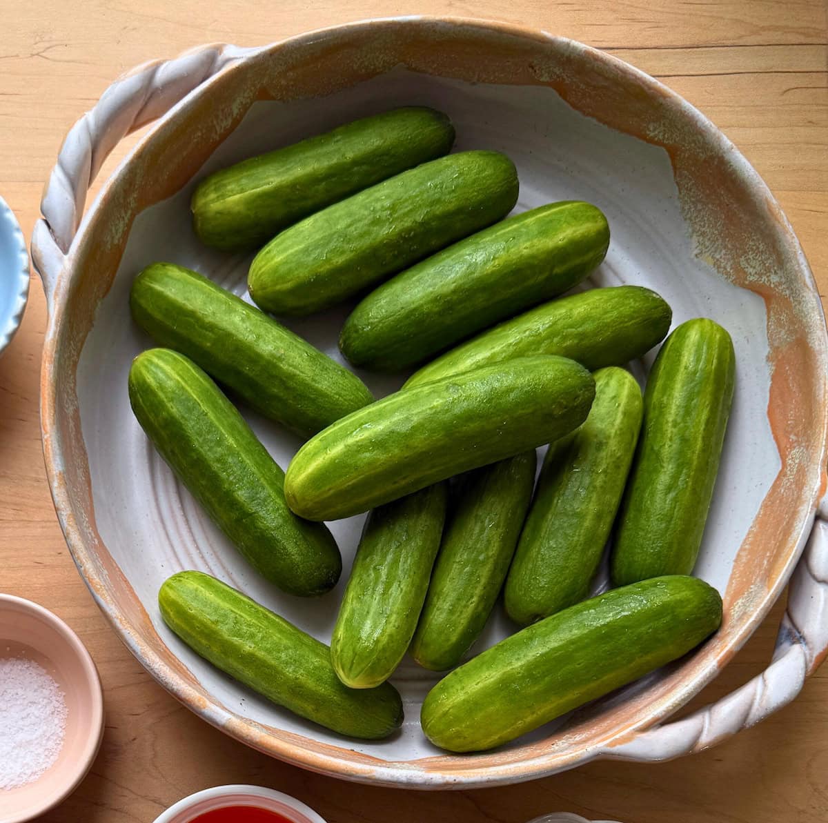 Several mini green cucumbers arranged in a rustic bowl on a wooden surface.