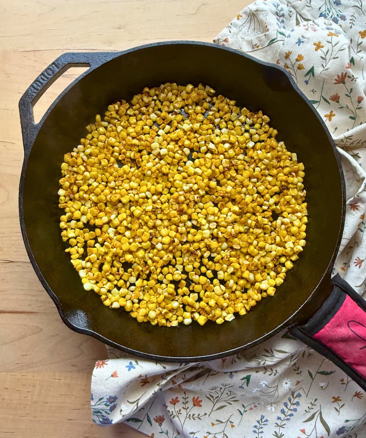 A close-up of toasted corn kernels in a cast iron skillet, with a floral-patterned cloth underneath.