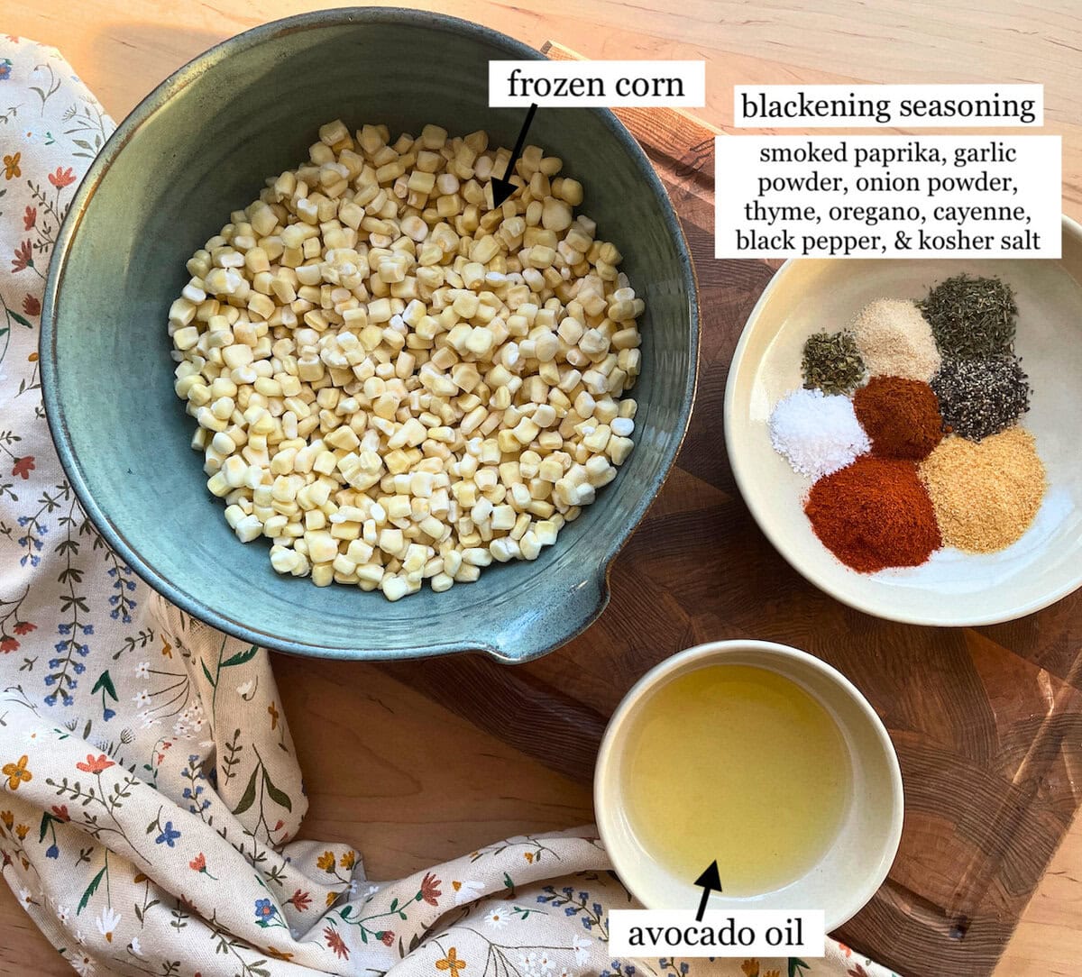 A bowl of frozen corn alongside a plate of assorted spices for blackening seasoning, including smoked paprika, garlic powder, and avocado oil.