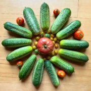 A circular display of cucumbers, tomatoes, and small yellow tomatoes on a wooden surface.