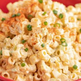 A close-up of a creamy macaroni salad topped with paprika and green onions, served in a red bowl.