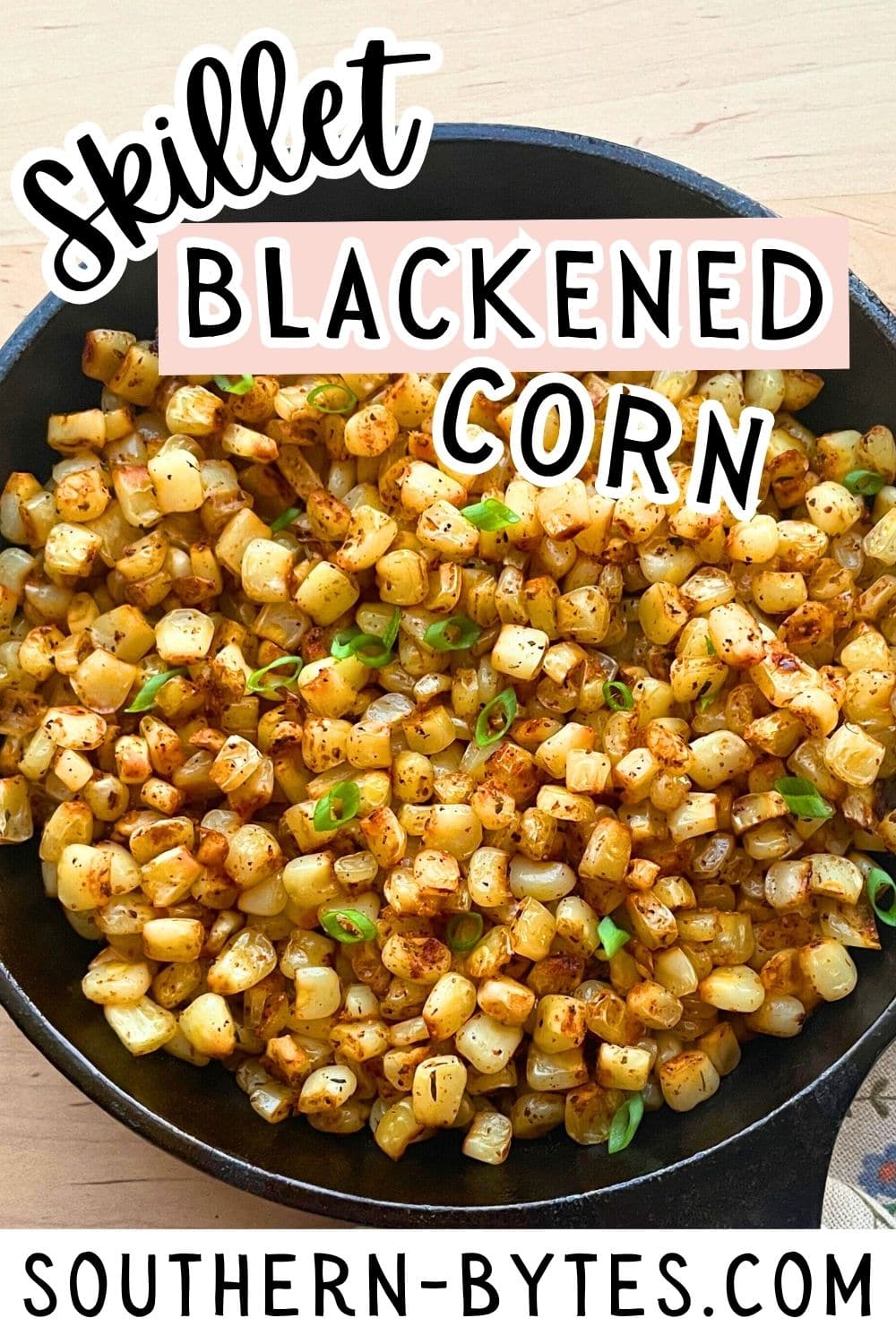 A close-up view of skillet blackened corn with green onions, presented in a cast iron skillet on a wooden surface.