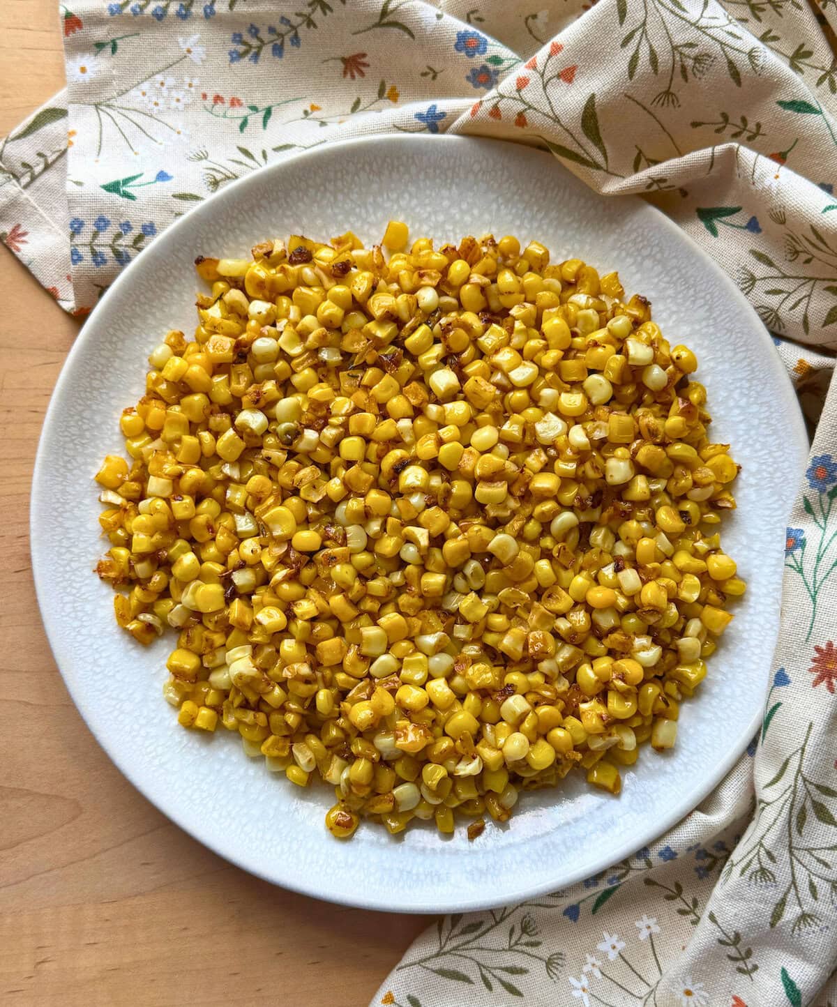 A plate of sautéed corn with a golden hue, surrounded by a floral-patterned napkin.