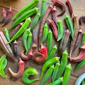 An assortment of green and reddish-purple okra pods displayed on a wooden table, showcasing their unique shapes and textures.