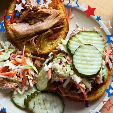 A close-up of a pulled pork sandwich topped with coleslaw and pickles, accompanied by a side of coleslaw and pickle slices, all framed by a festive star border.