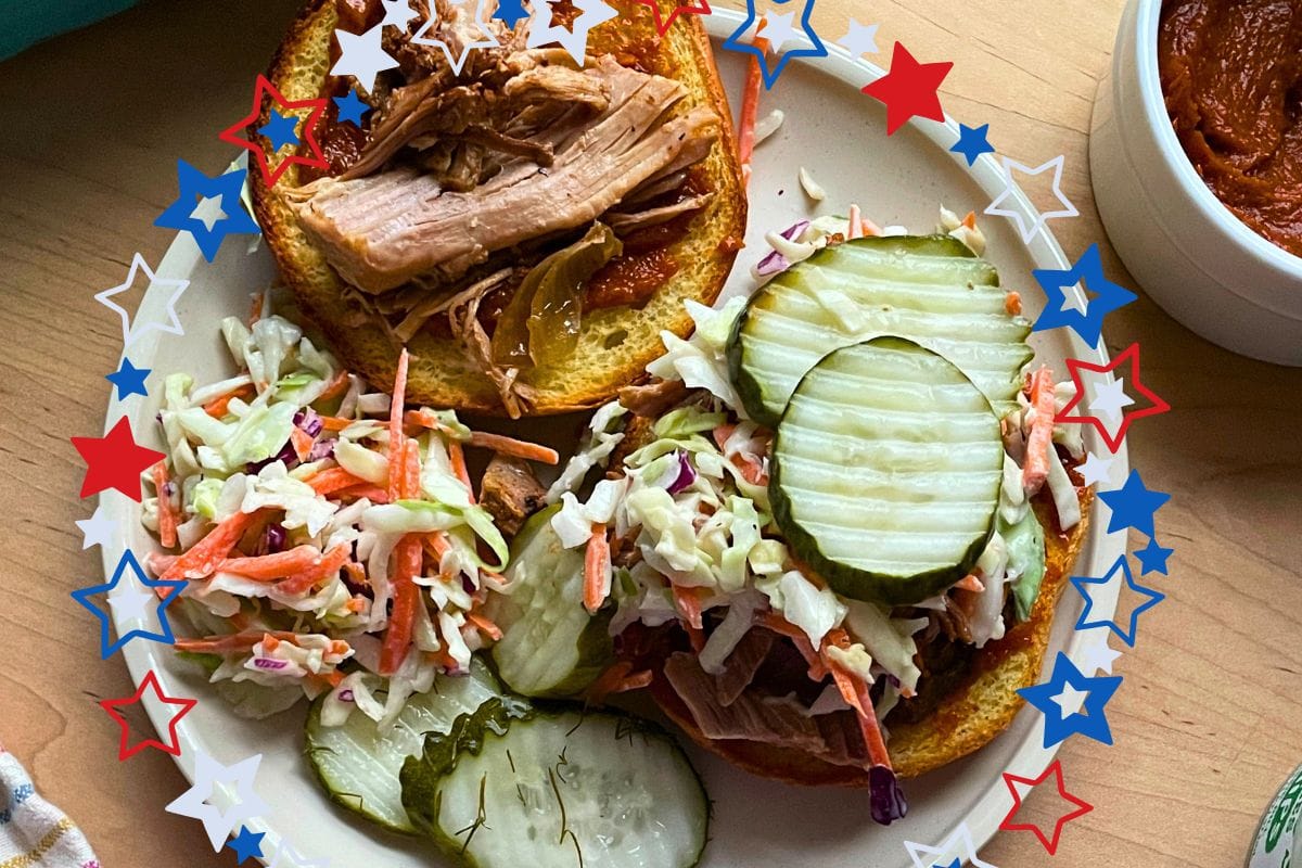 A close-up of a pulled pork sandwich topped with coleslaw and pickles, accompanied by a side of coleslaw and pickle slices, all framed by a festive star border.