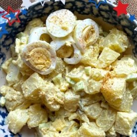 A colorful bowl of potato salad topped with sliced hard-boiled eggs and sprinkled with seasoning, set against a backdrop of decorative stars.