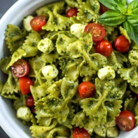 A vibrant bowl of farfalle pasta mixed with basil pesto, cherry tomatoes, and mozzarella balls, garnished with fresh basil leaves.