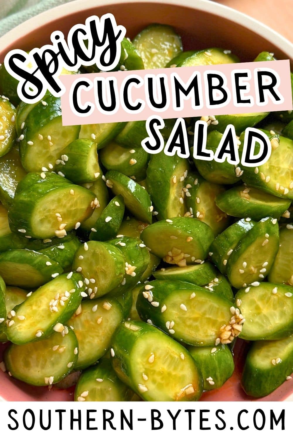 Close-up of a pink bowl of spicy cucumber salad garnished with sesame seeds.